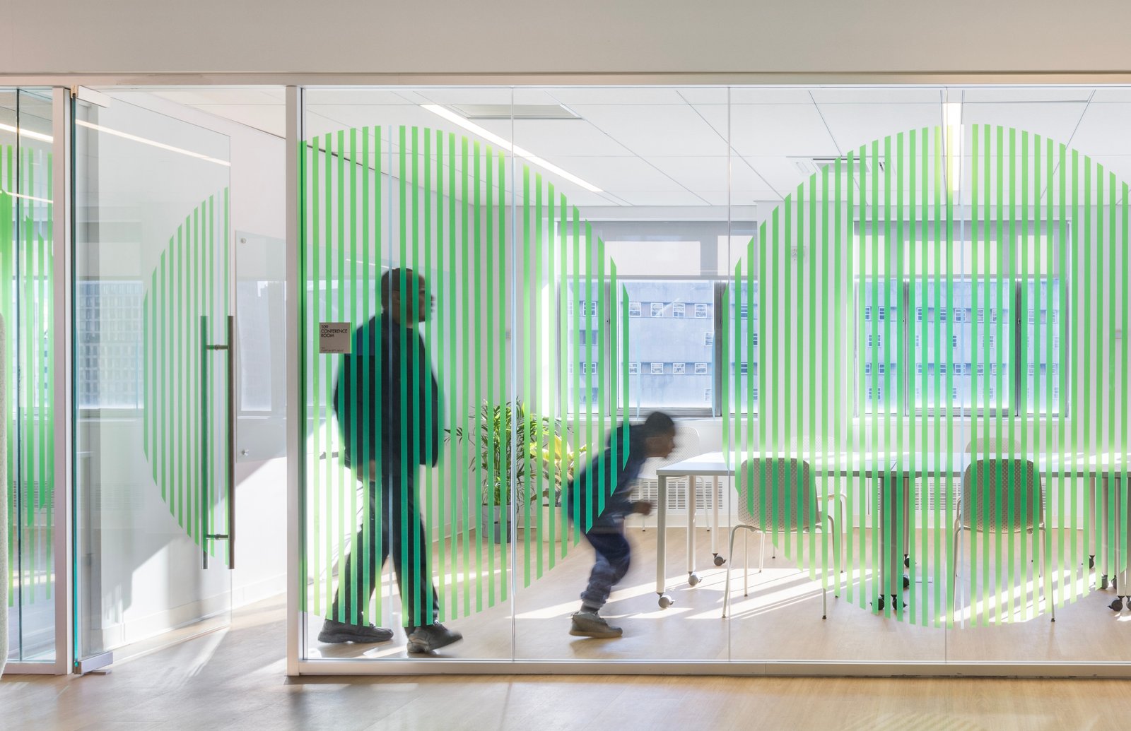 Glass meeting room with green striped partitions and natural light.